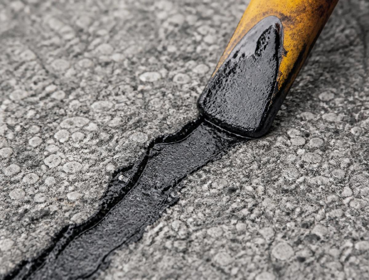 Close view of hot rubber crack sealant being applied to asphalt